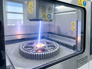Laser Powder Bed Fusion (LPBF) 3D printing machine fabricating a large 42CrMo steel gear with a blue laser beam.