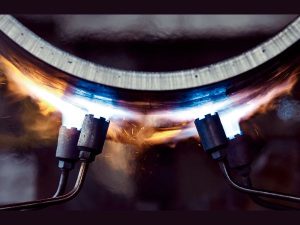 High-temperature industrial torches heating a curved metal part during post-processing heat treatment to relieve stress and refine microstructure.