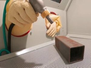 Operator performing sandblasting on a metal part during metal 3D printing post-processing